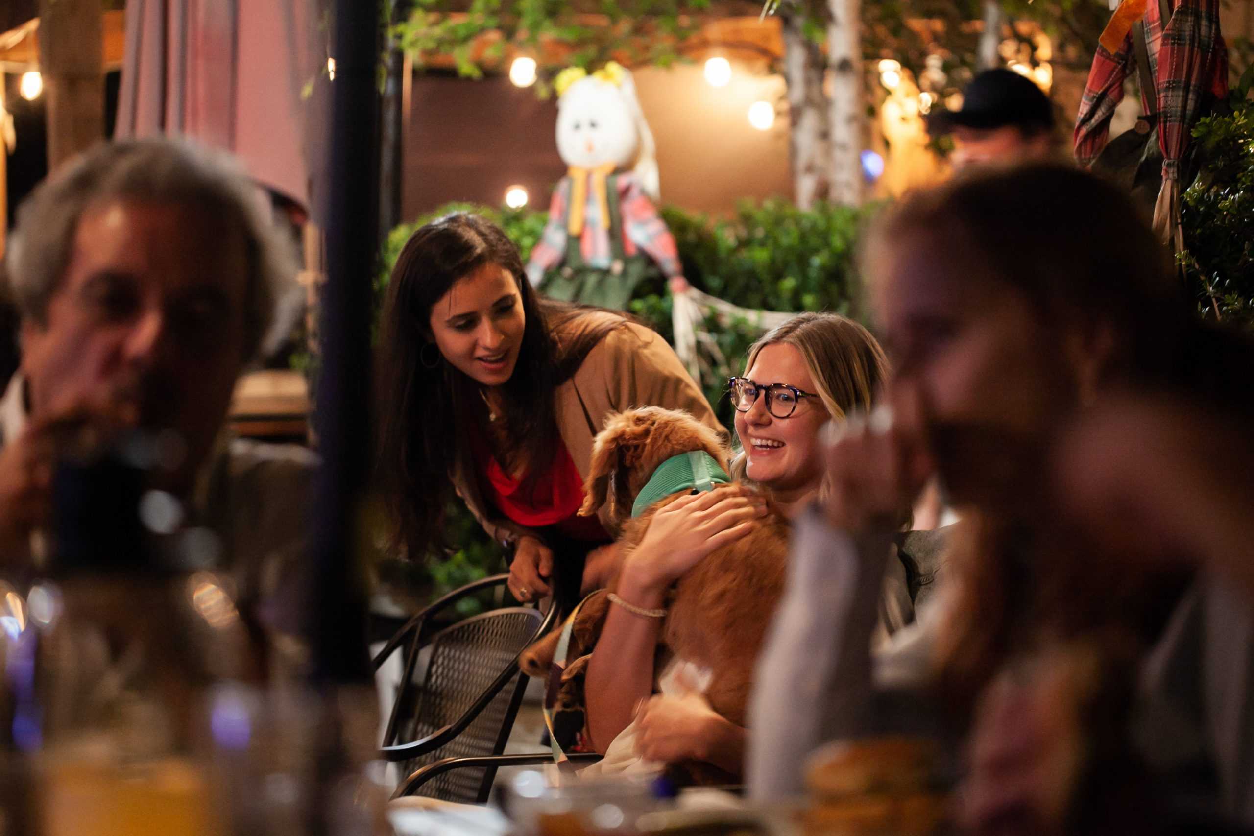 A photo focused on two people smiling over a dog at a party, one person is holding the dog.