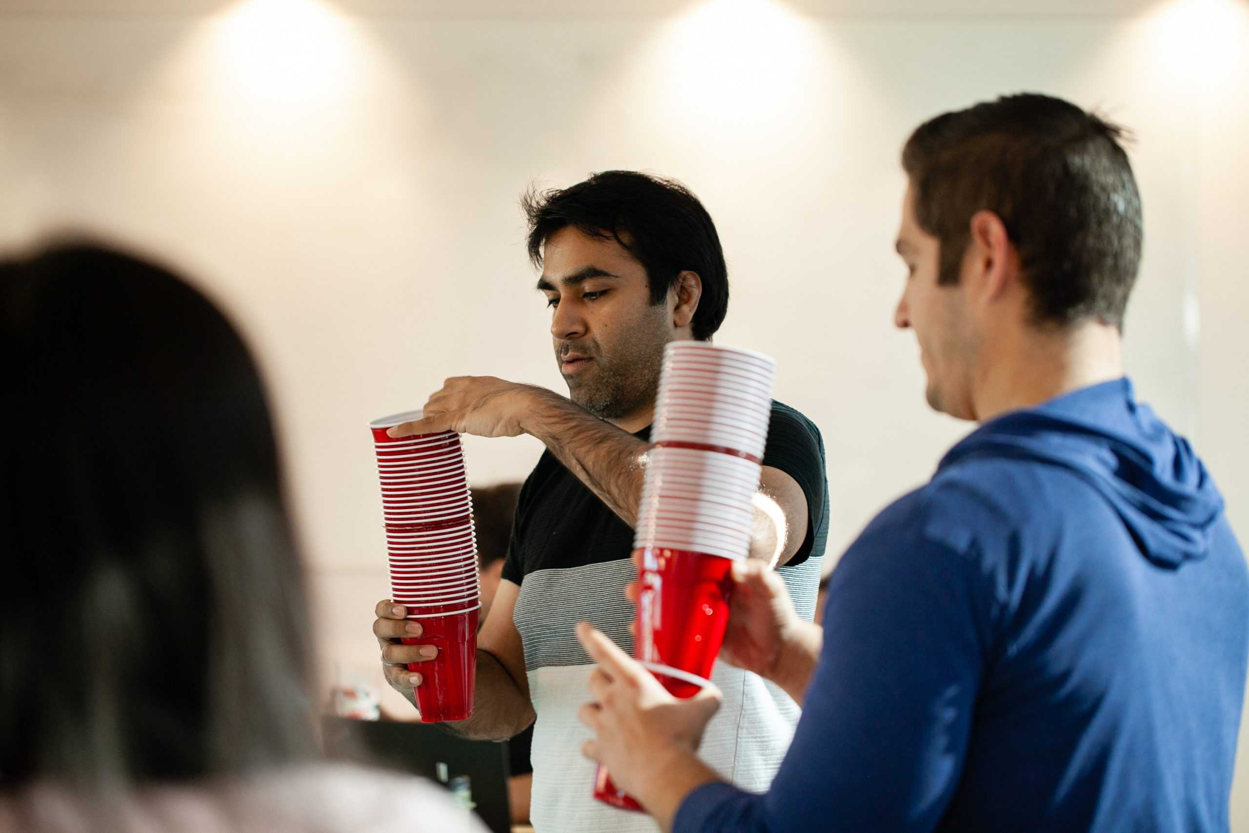 Two people each holding a tall stack of red solo cups and focusing.