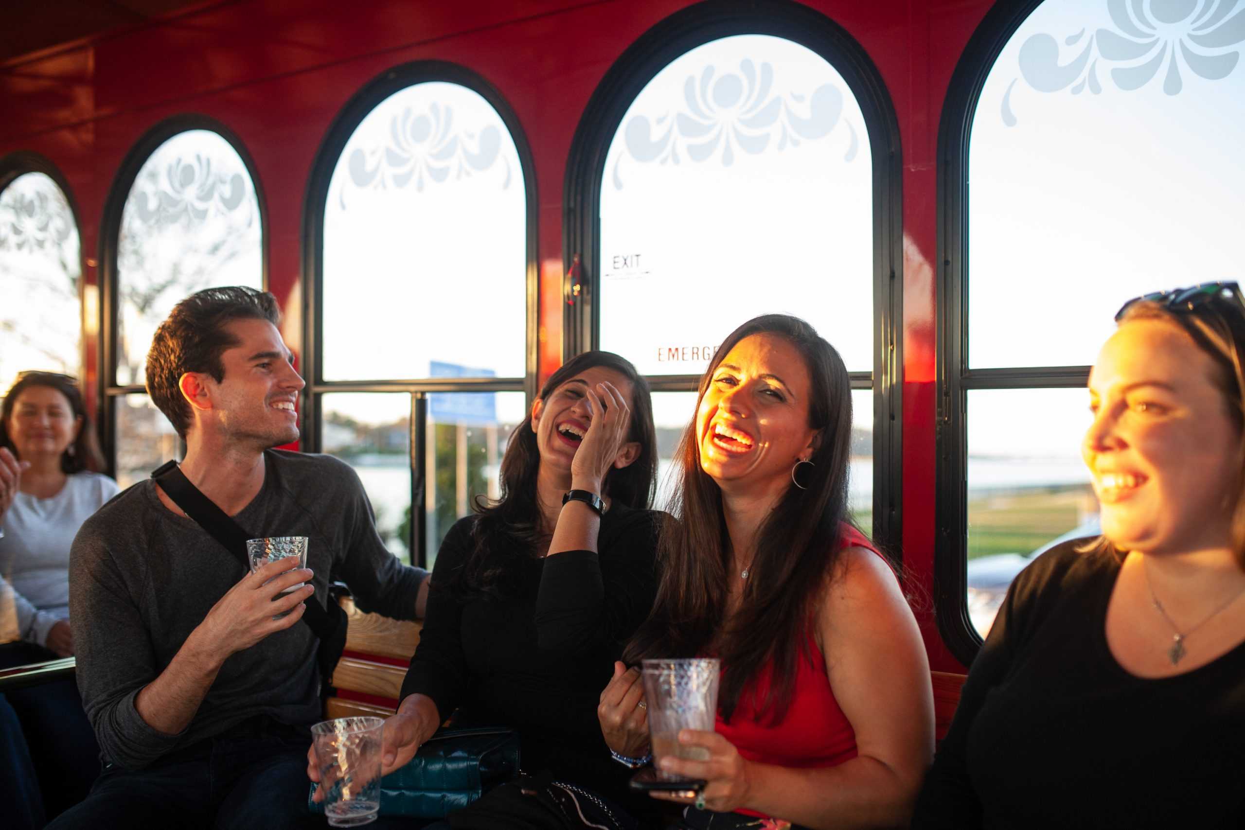 A group of four people drinking and laughing heartily while sitting in a trolley car.
