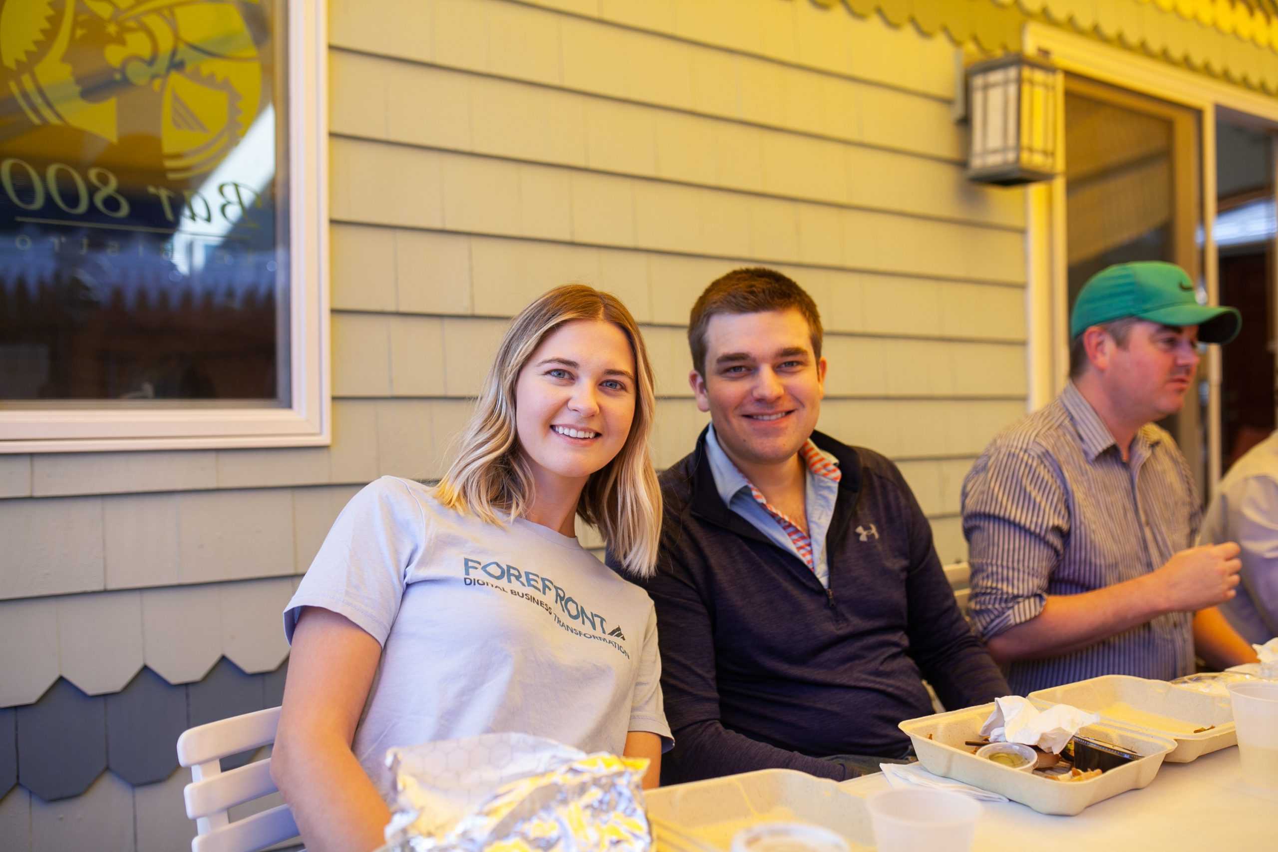 Three people dining outdoors, with a woman and a man smiling at the camera.