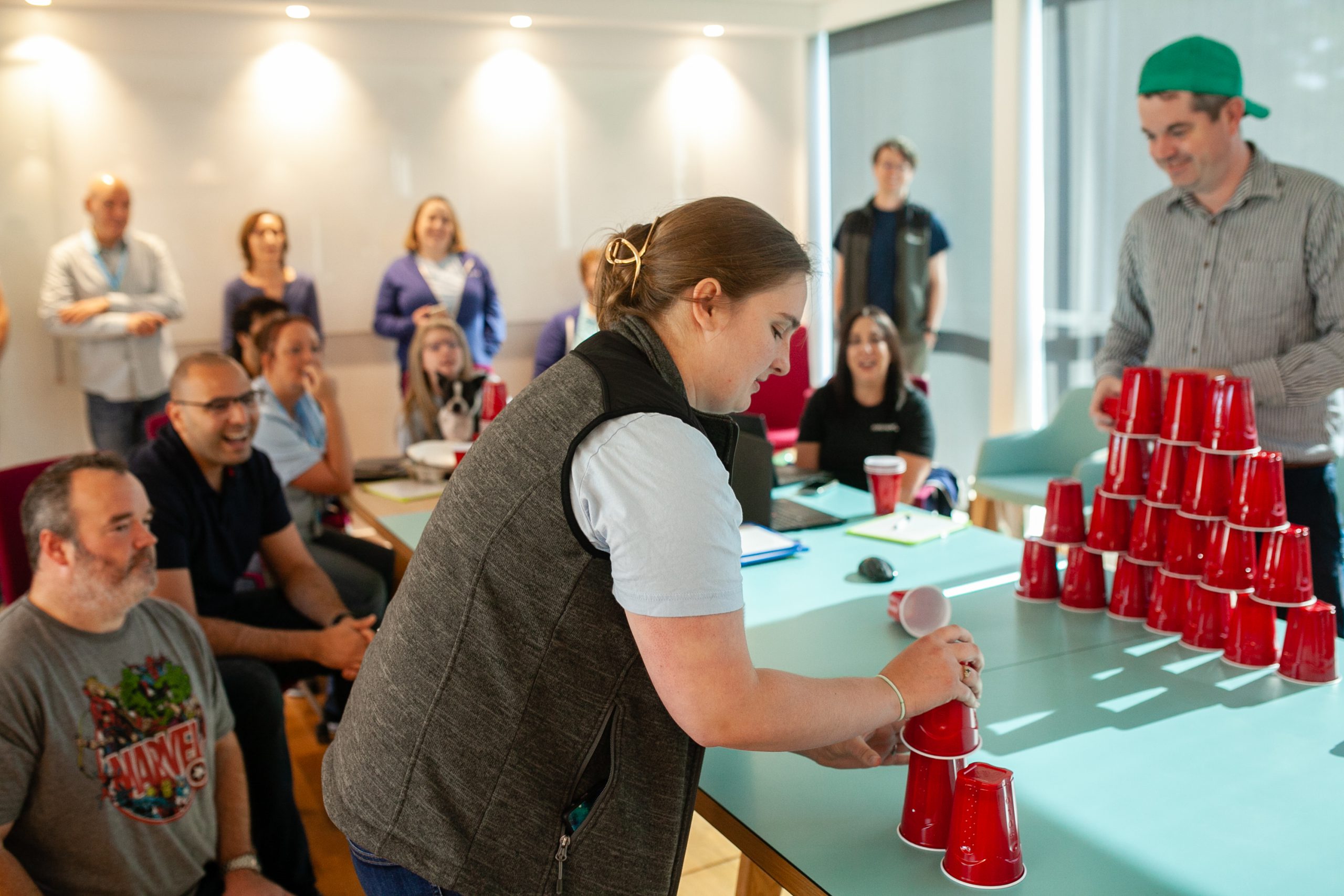 4FDay_2021_20-scaled Two people compete in a game, stacking red solo cups into a pyramid, while onlookers watch.