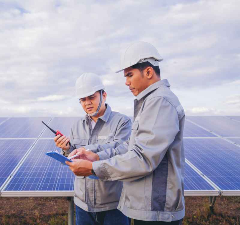 Two men in hard hats inspecting solar panels at a solar farm.