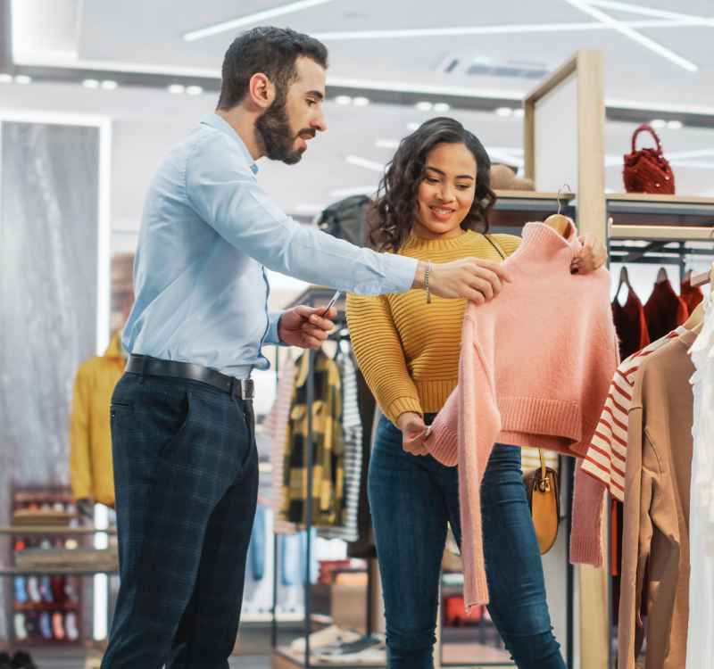 A man and woman browsing through racks of clothes in a boutique.
