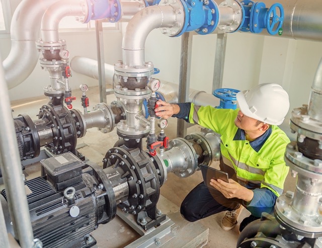 A worker at a water station is closing a water pipe valve in a large industrial estate. Water pipes. Industrial plumbing.