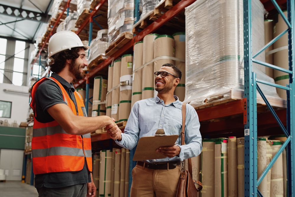 Cheerful,Young,Business,Man,In,Formal,Clothing,Wearing,Side,Bag Cheerful young business man in formal clothing wearing side bag and holding clipboard making handshake gesture with warehouse manager - two business partners making a deal